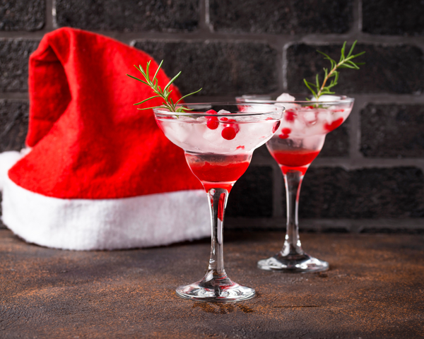 Two cocktail glasses with cranberries and a red Santa hat