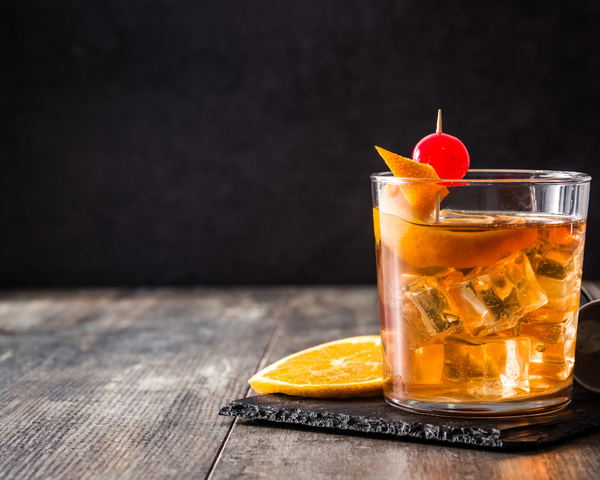 Glass sitting on black coaster with a slice of orange and cherry