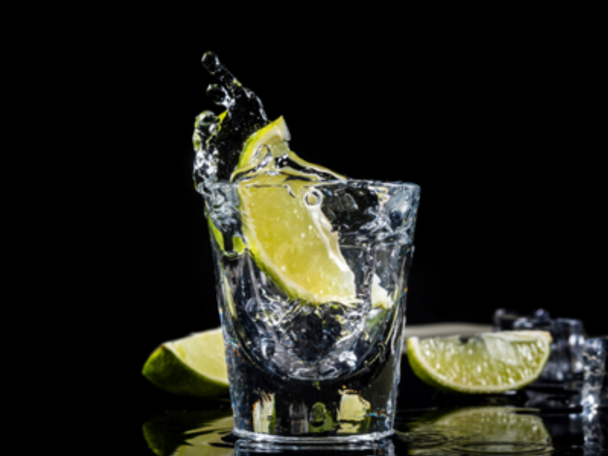 Glass of silver tequila with a wedge slice splashing