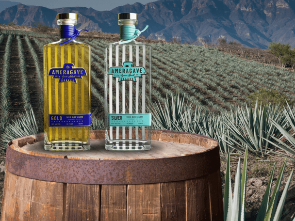 Bottles of Ameragave sitting on a barrel in front of a field of agave