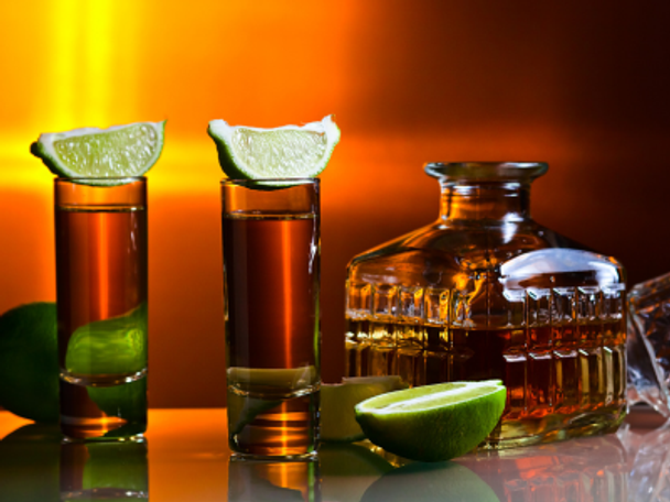 Two shot glasses with lime wedges next to a bottle of tequila