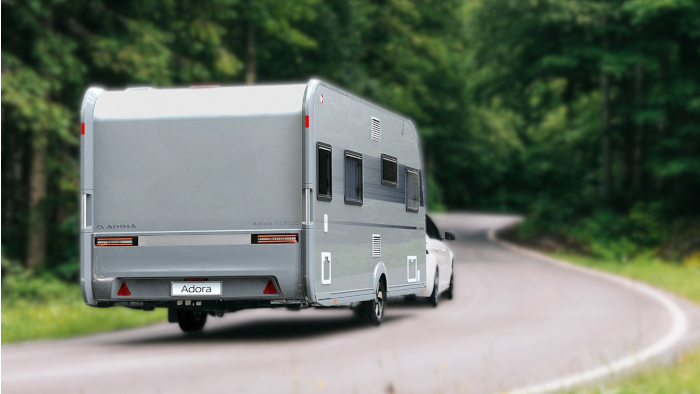 An Adria Adora caravan being towed on a windy road through the forest