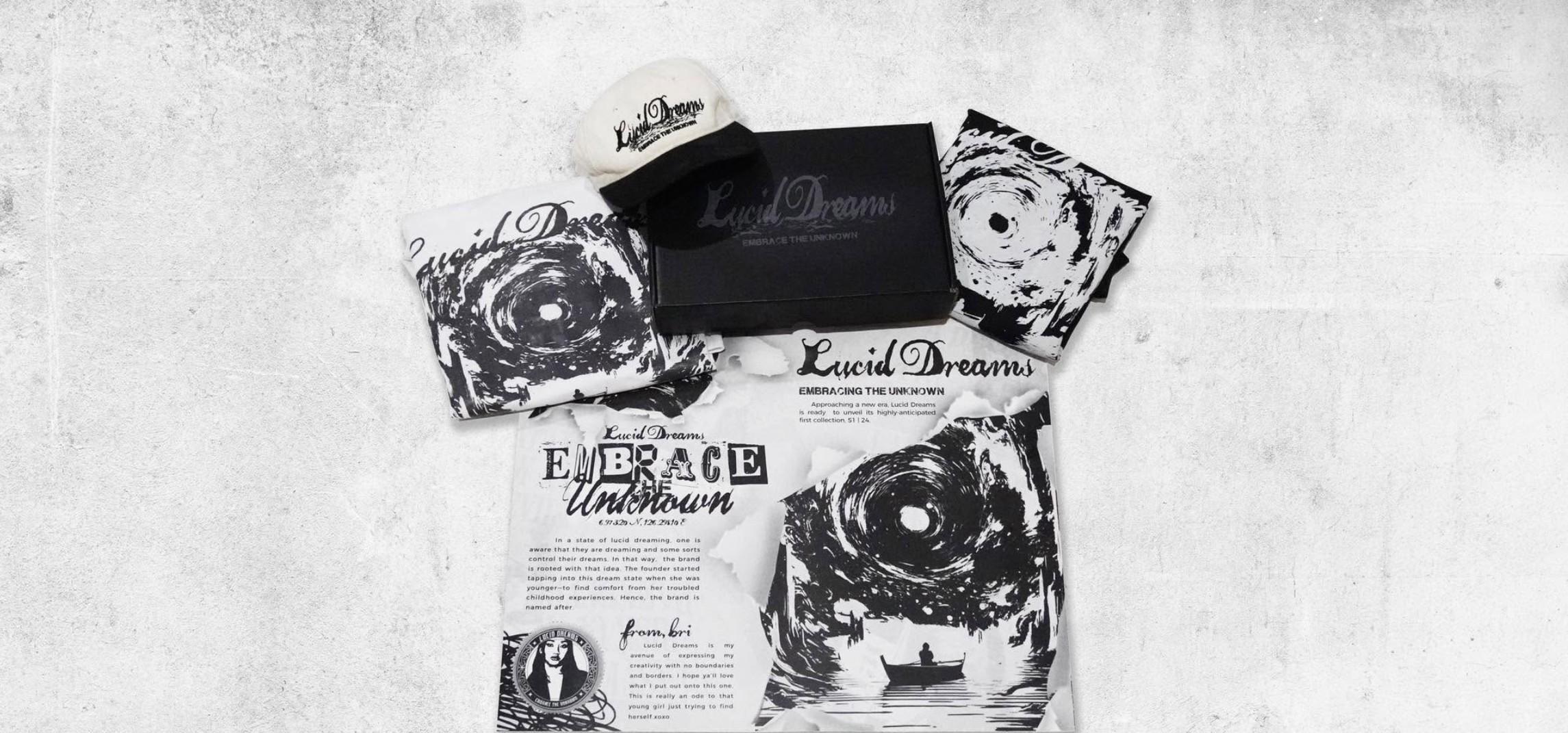 The S1 | 24 collection laid out on concrete: vortex-print tees, a two-tone cap, the black mailer box and the Embrace the Unknown zine with Bri’s note
