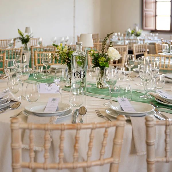 Mesa redonda com runner verde, jarras de flores e menus
