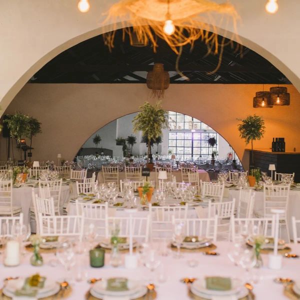 Salão de casamento com arcos, cadeiras brancas e mesas postas