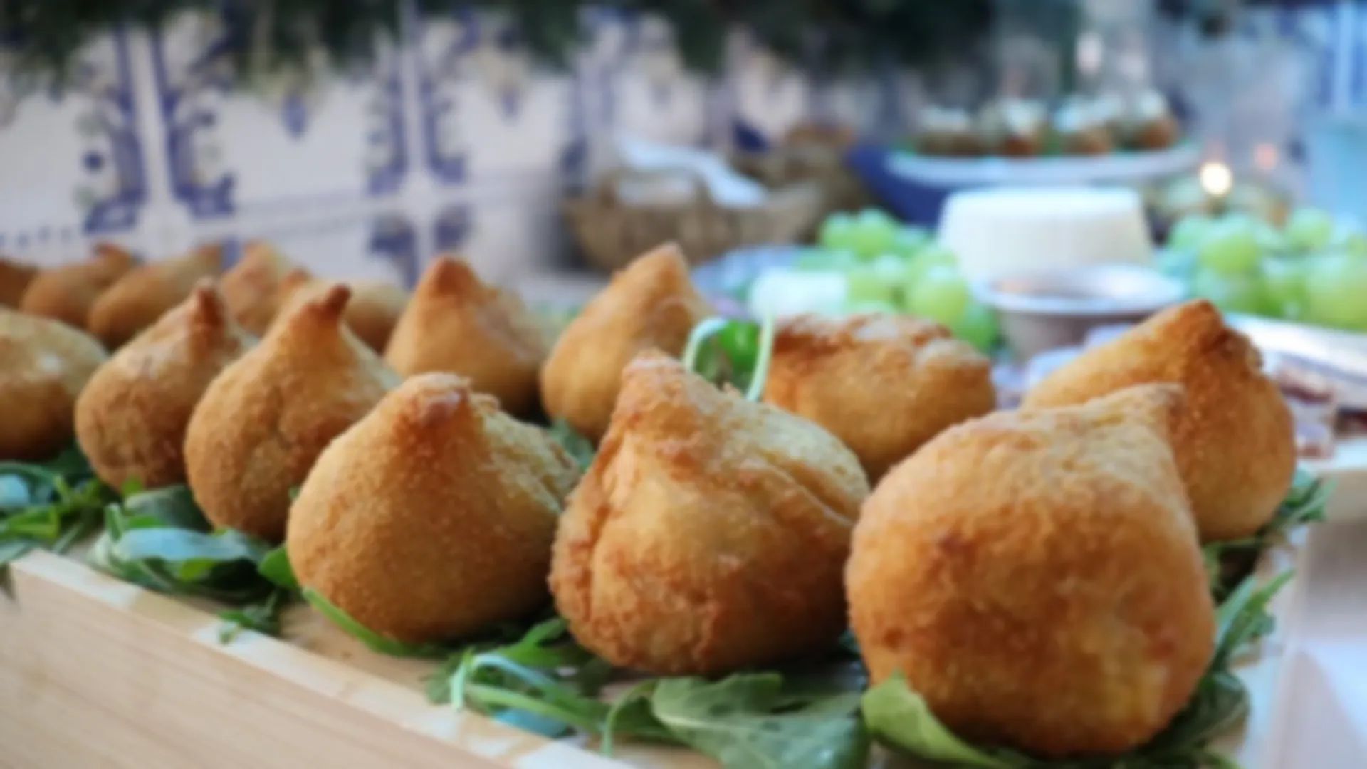 Coxinhas douradas sobre rúcula num buffet com azulejos ao fundo