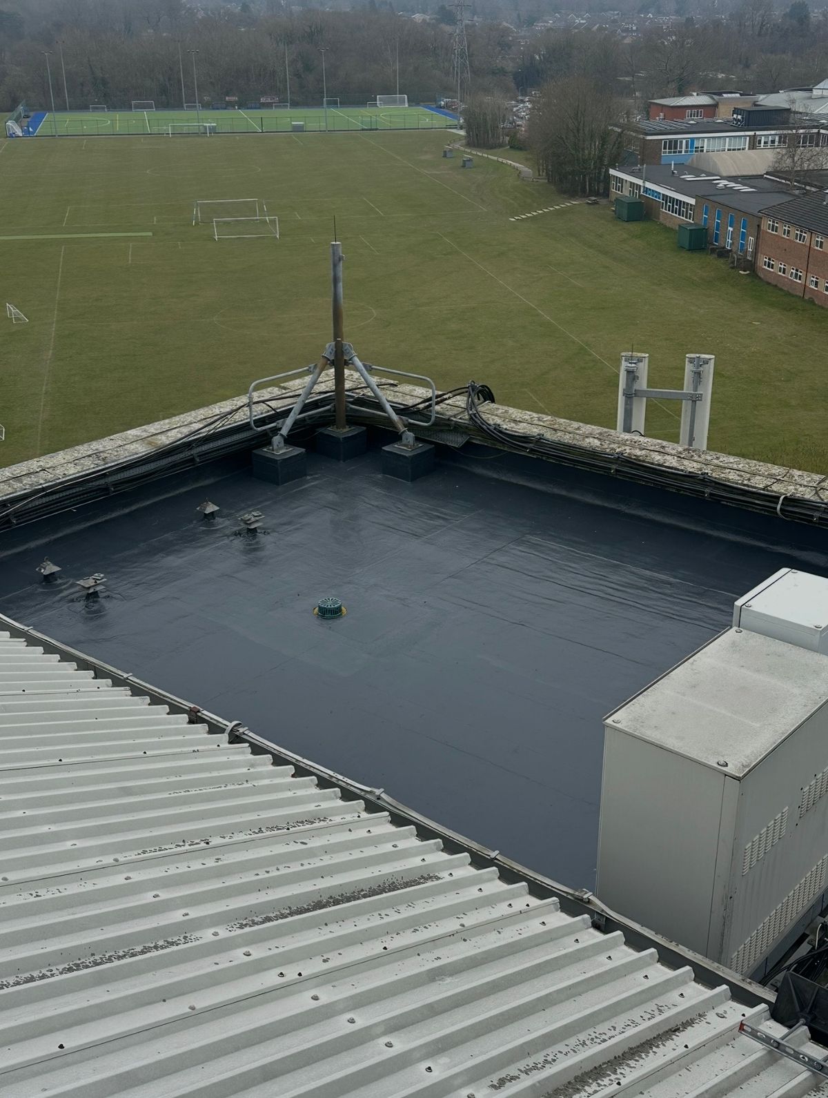 Wide view of the completed liquid waterproofing system across the commercial flat roof and perimeter upstands.