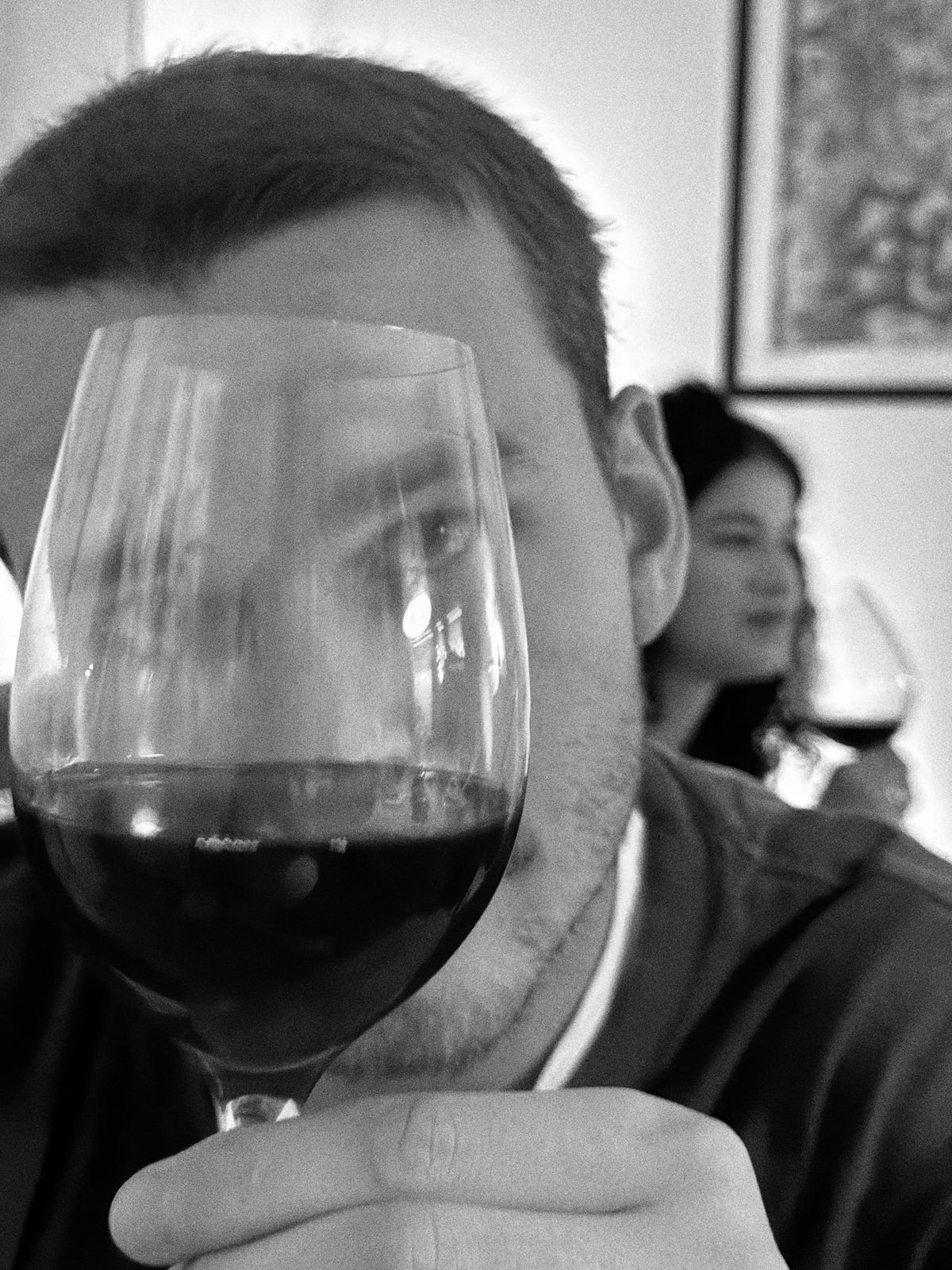 Black-and-white photo of a man looking into a glass of red wine at a dinner table