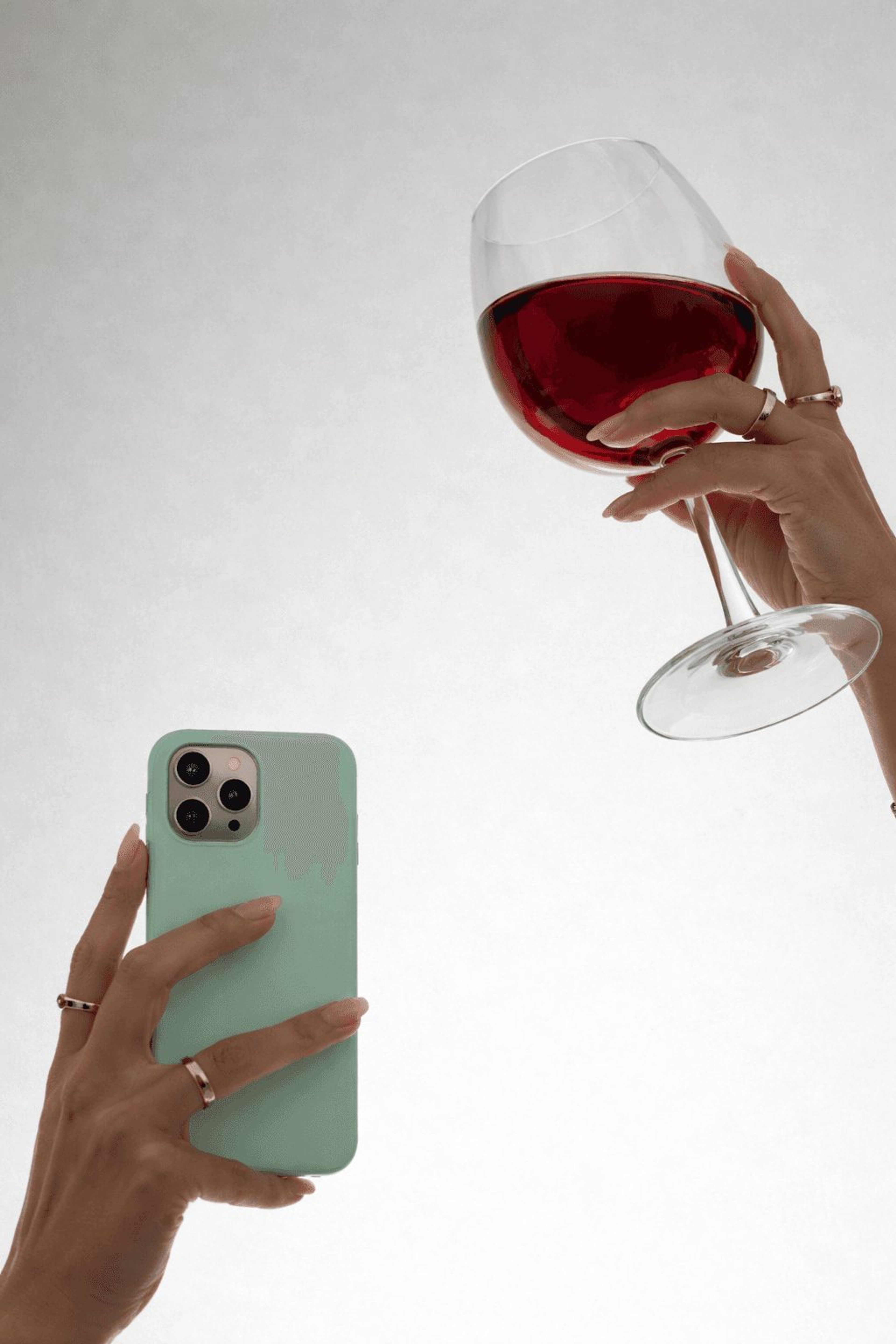 Hand holding a glass of red wine next to a smartphone ready to scan the label
