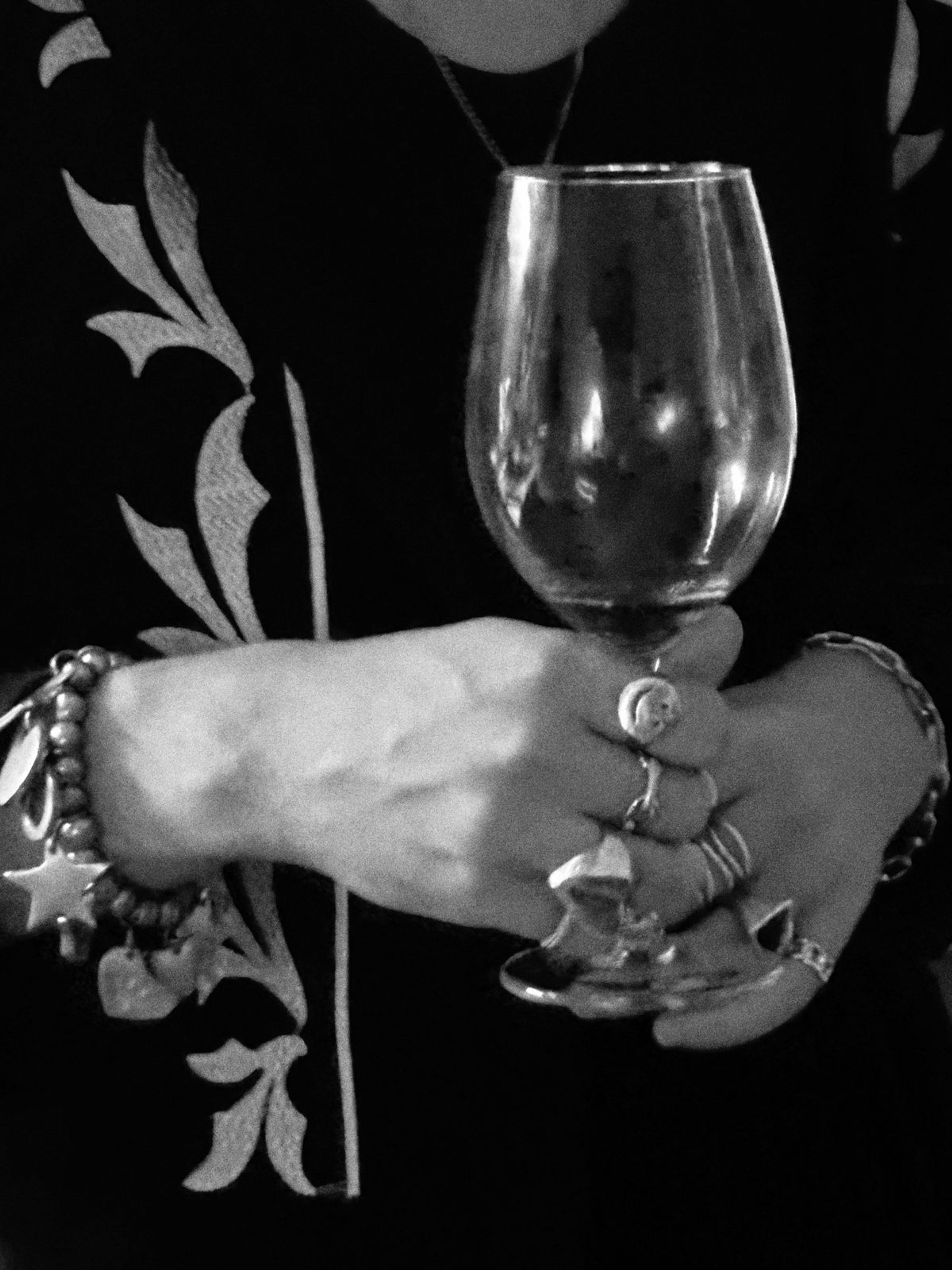 Black-and-white close-up of a hand with rings holding a glass of red wine
