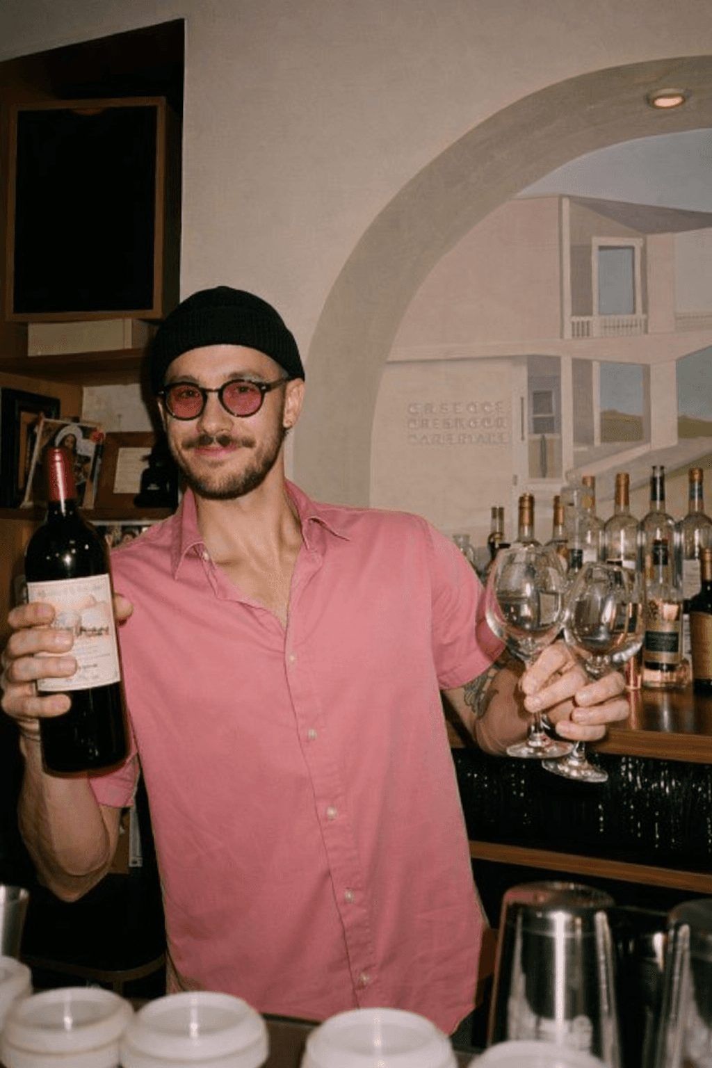 Bartender holding a bottle of red wine and glasses behind the bar