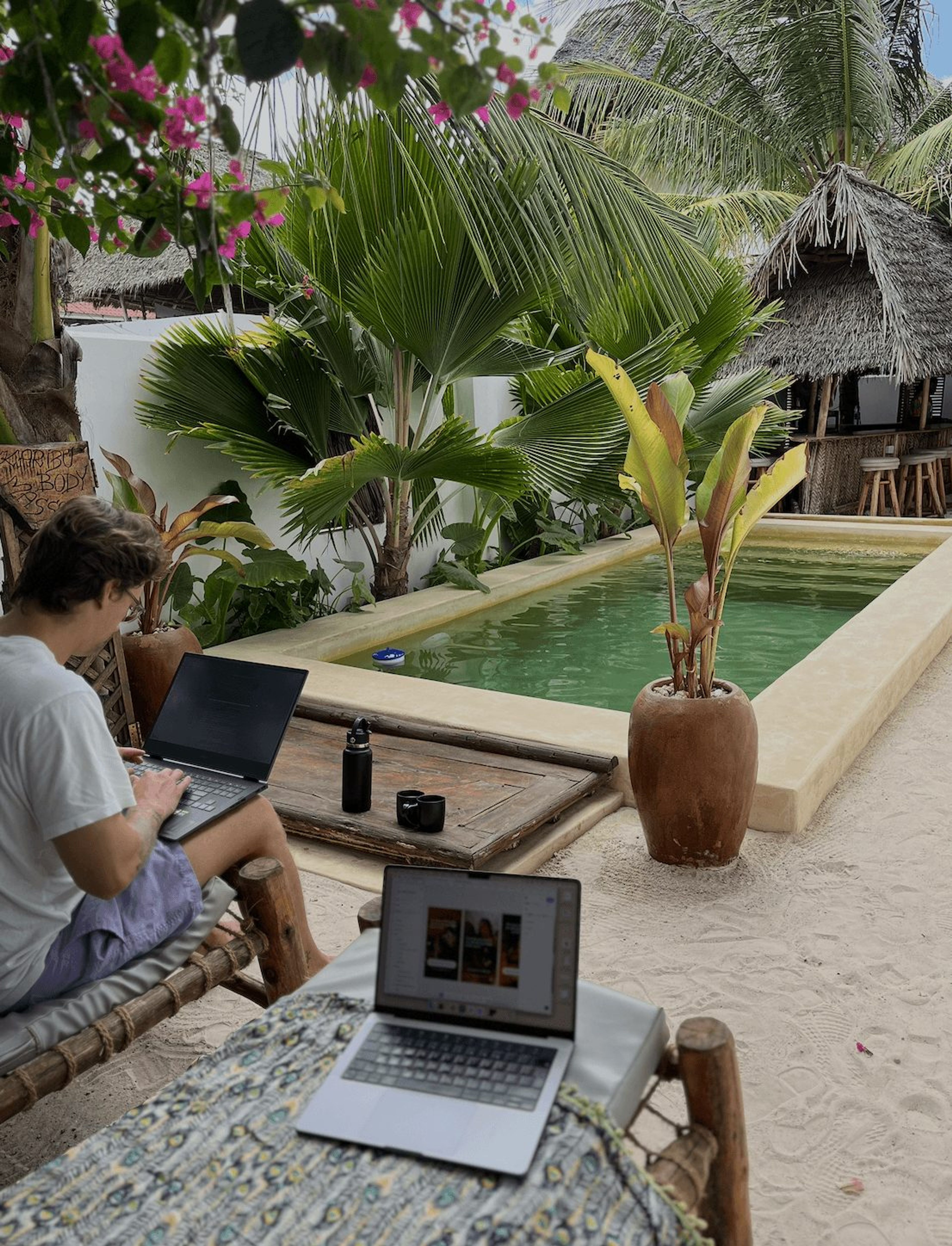 Laptops on a table beside a pool in a tropical garden