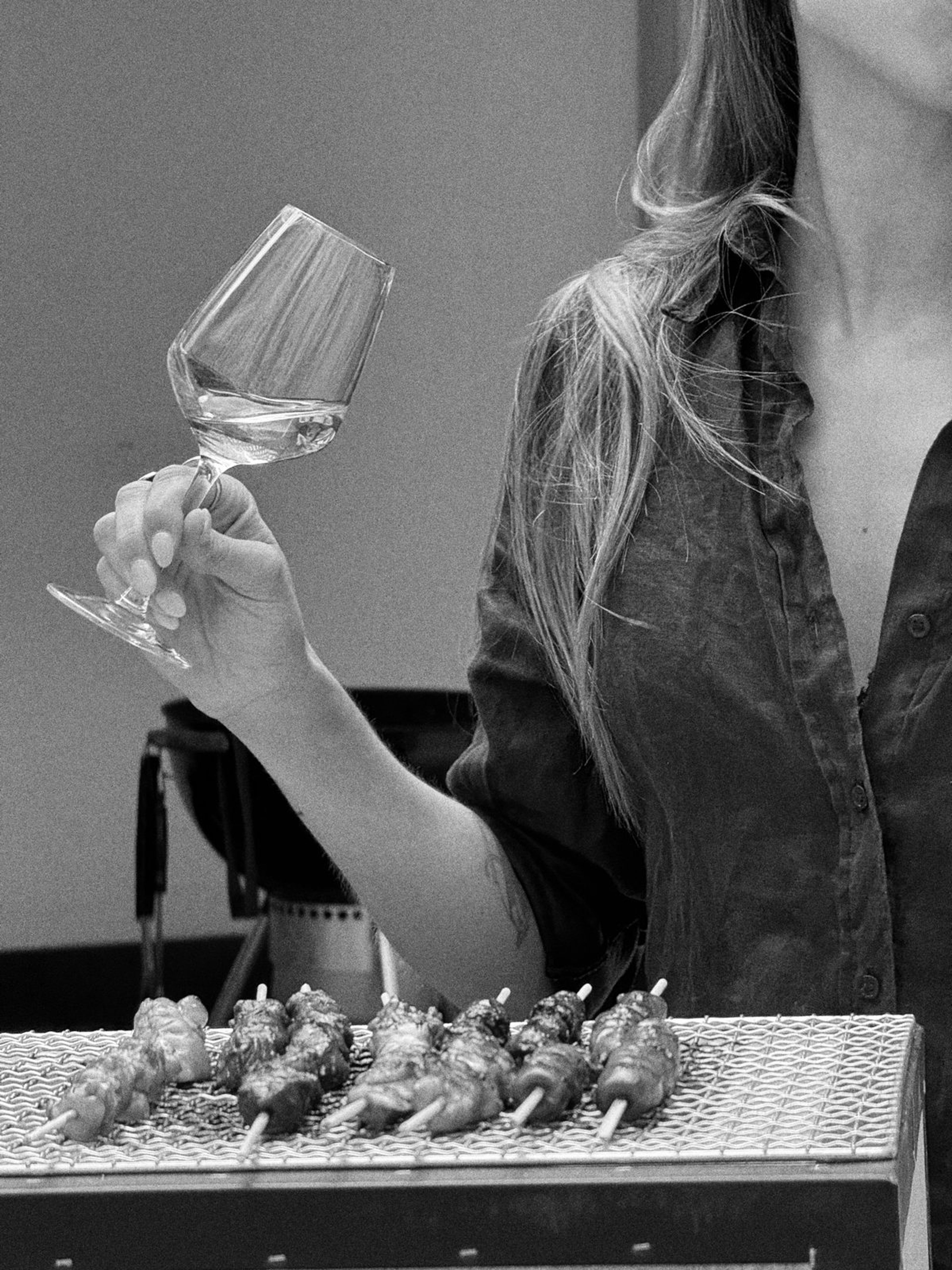 Black-and-white photo of a hand holding a glass of white wine next to a grill