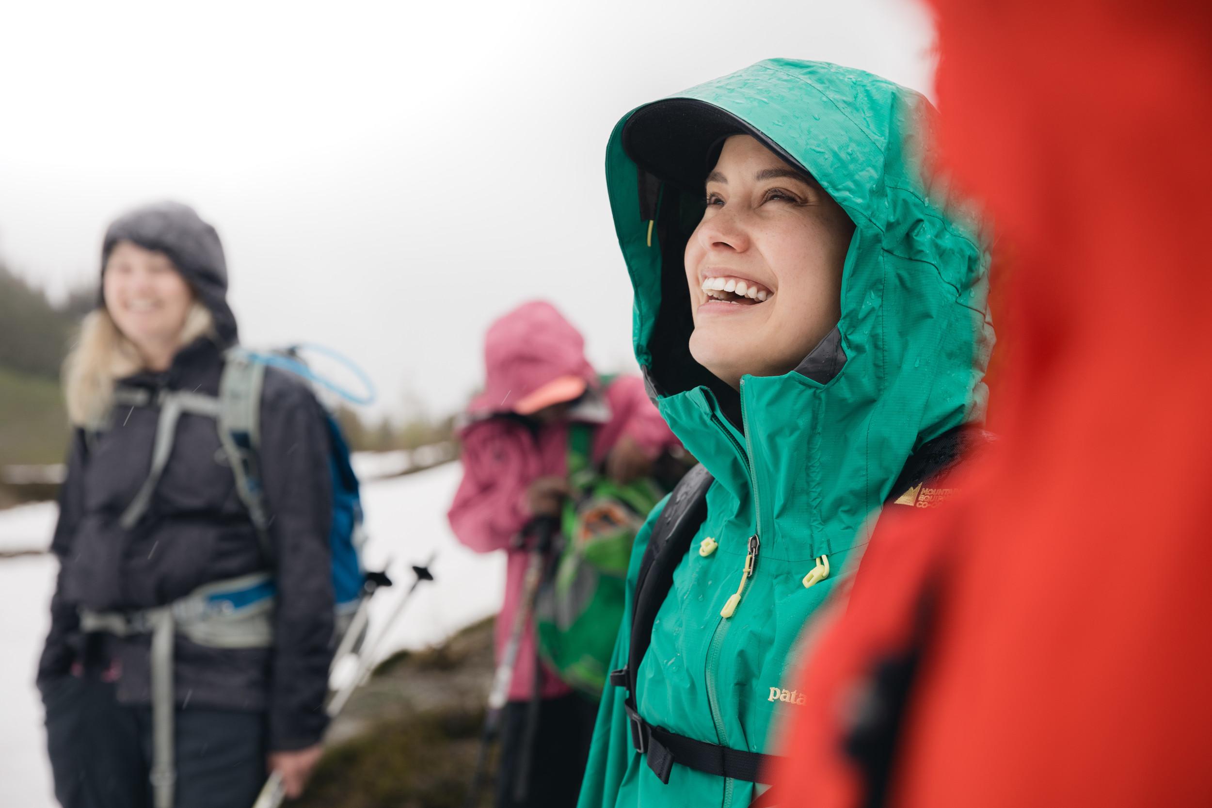 A woman in a green jacket smiling with people blurred in the background