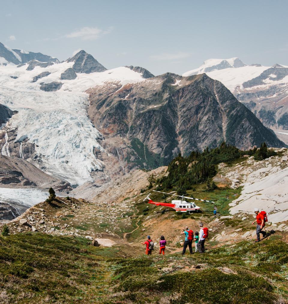 a group of people walking towards a helicopter with a glacier in the background