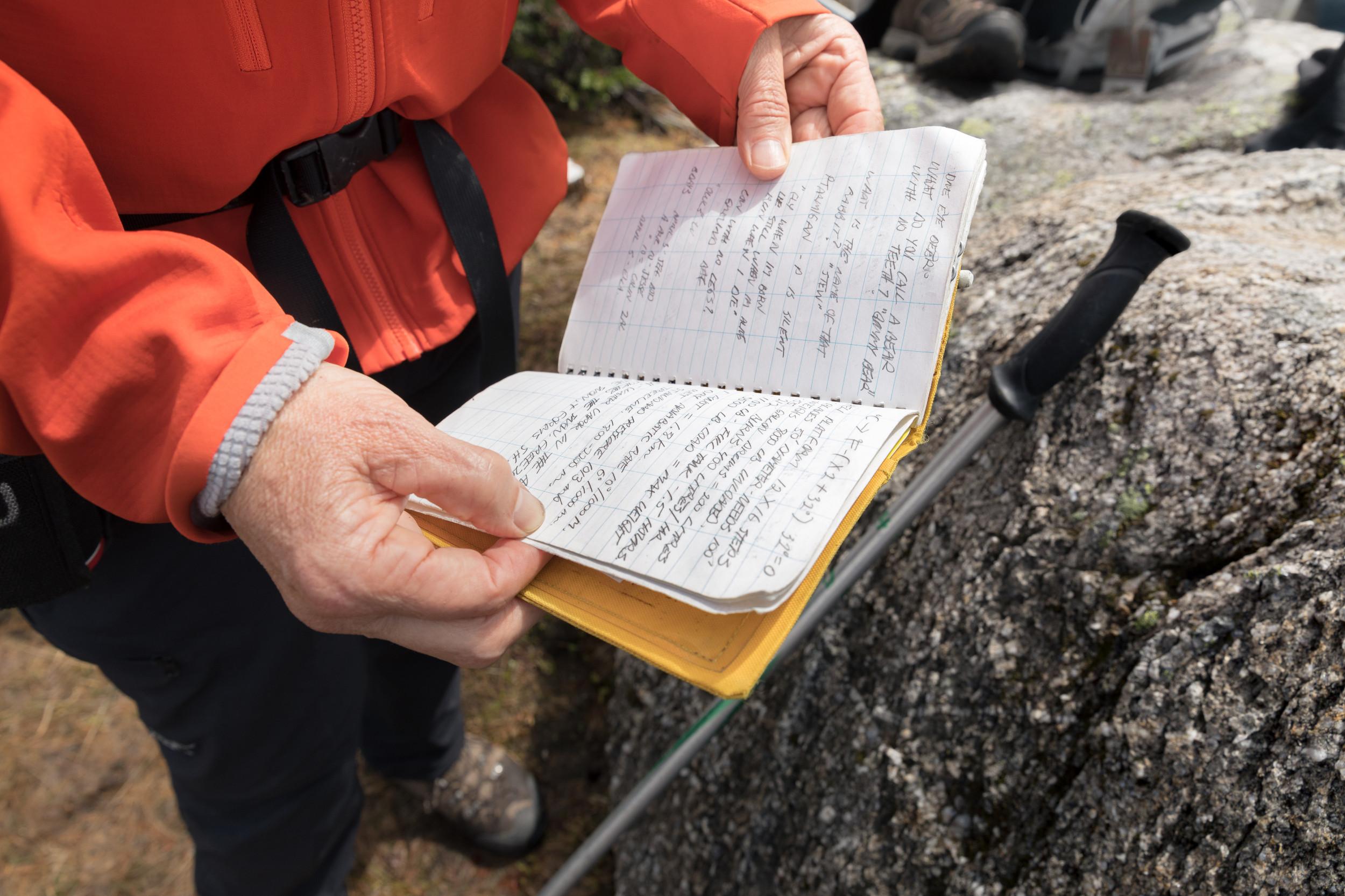 close up of a field notebook held by a person in an orange jacket against some rocks