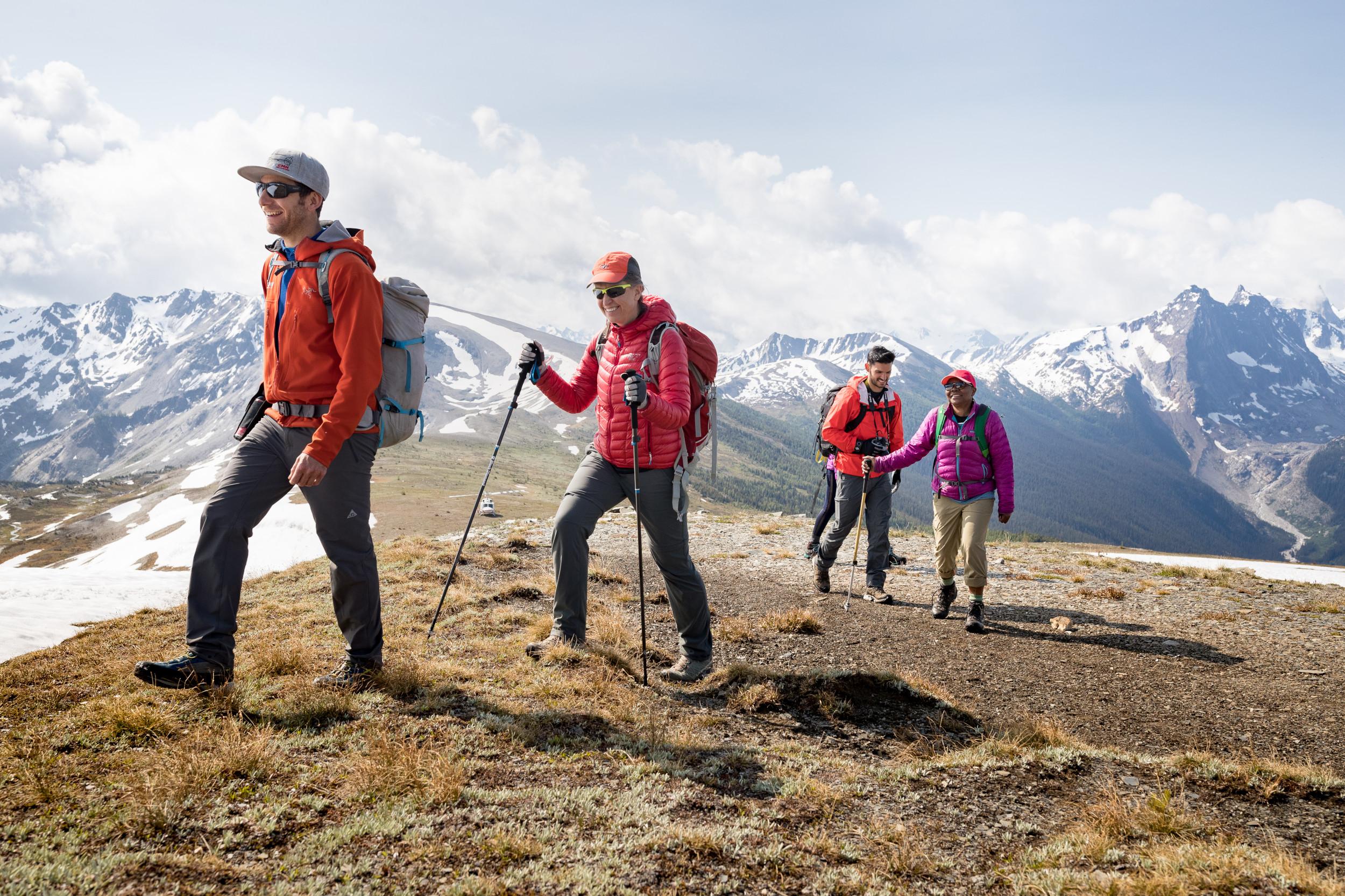 Four people walking in a row on a hill with mountains in the background