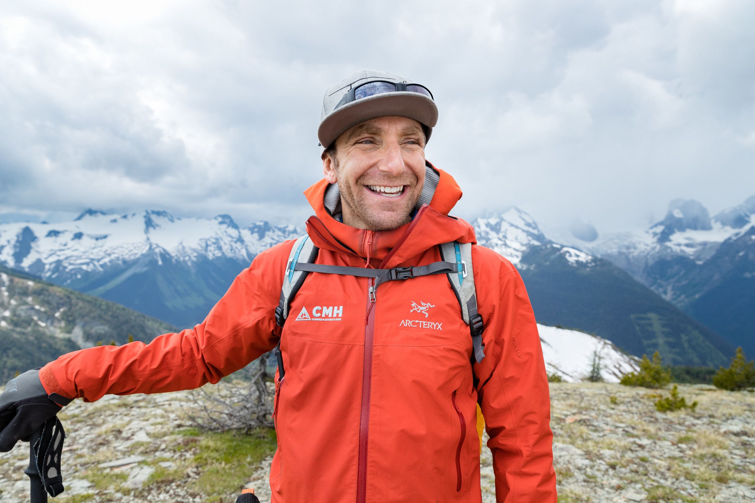 A man in an orange jacket smiling with mountains in the background