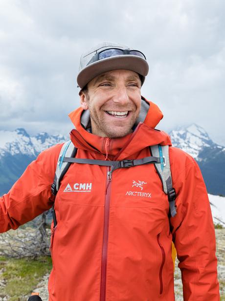 A man in an orange jacket smiling with mountains in the background