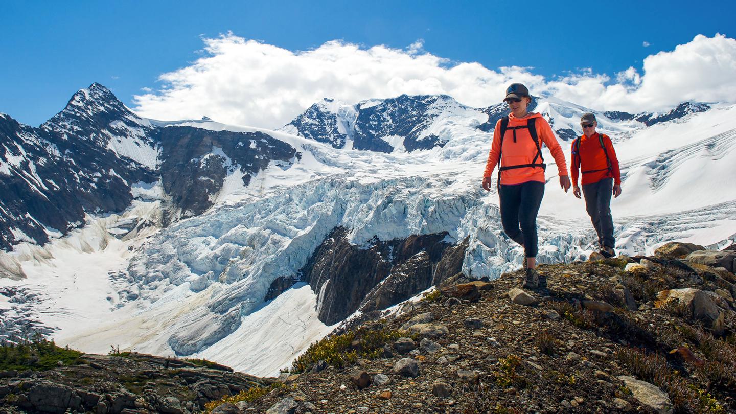 two people walking on a ridge with a glacier in the background