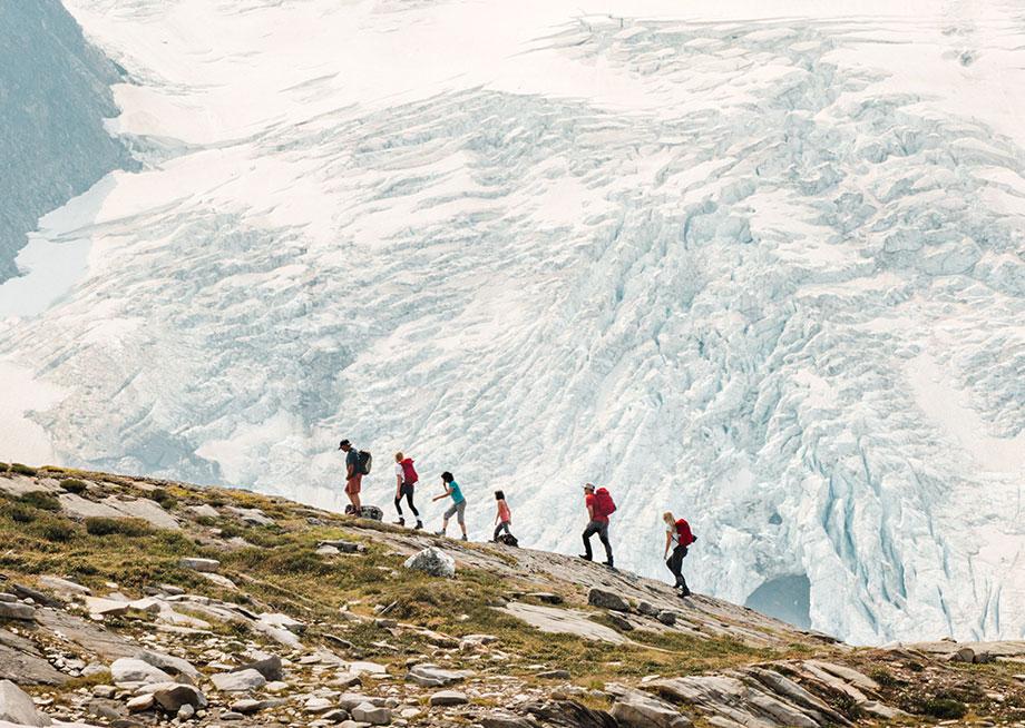 Group of hikers walking along a rocky slope with a glacier in the background.