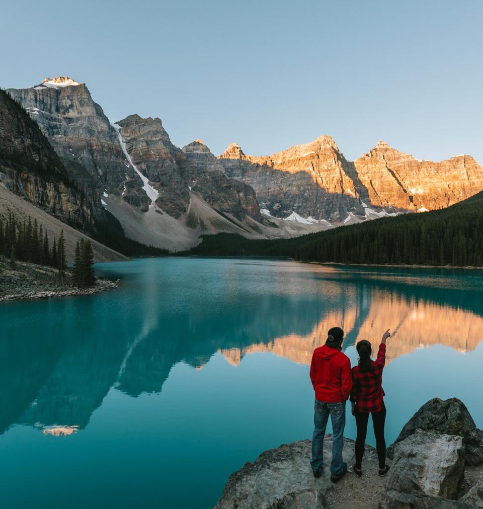 two people looking out on a calm lake with mountains in the background