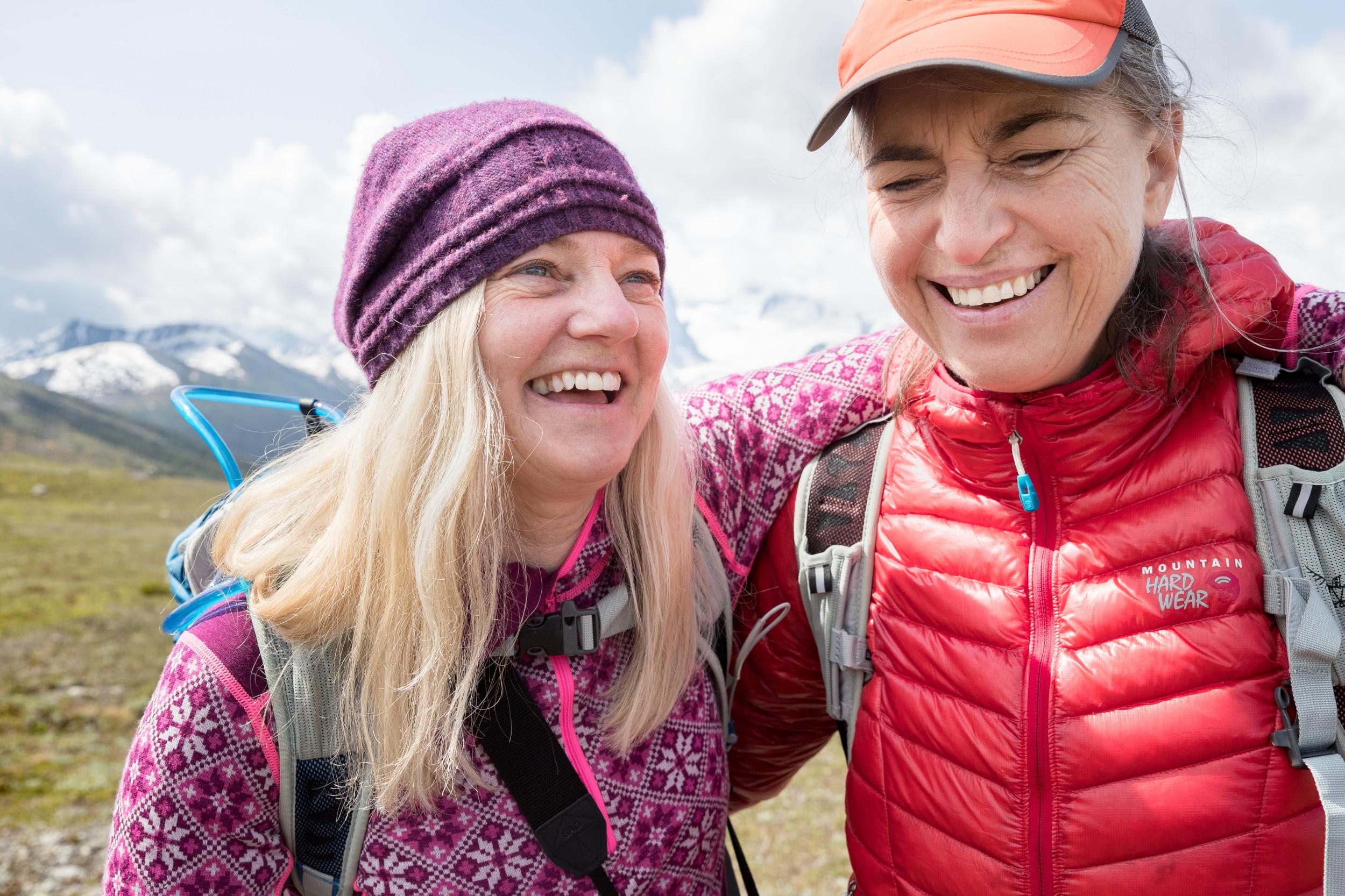 Two women in hiking clothing smiling, each with an arm around the other