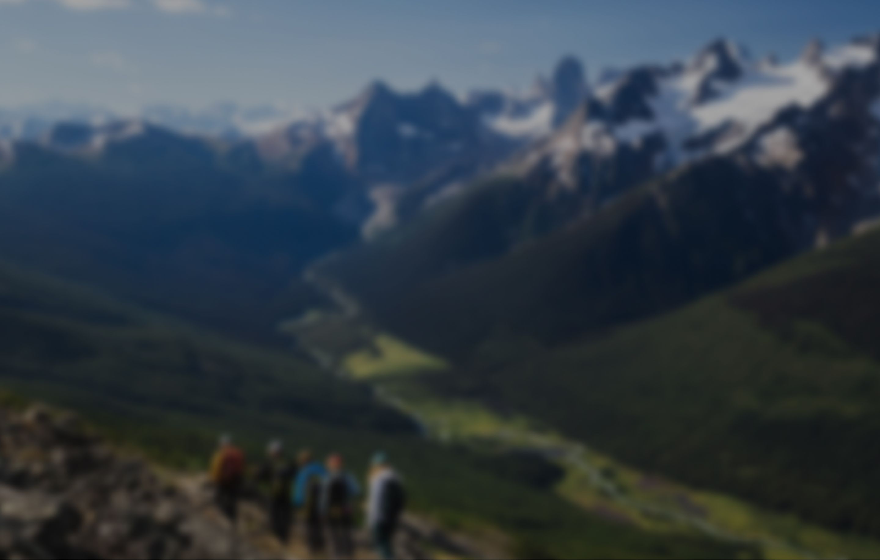 A group of people walking on a ridge with lush forest and a river below and mountains in the background