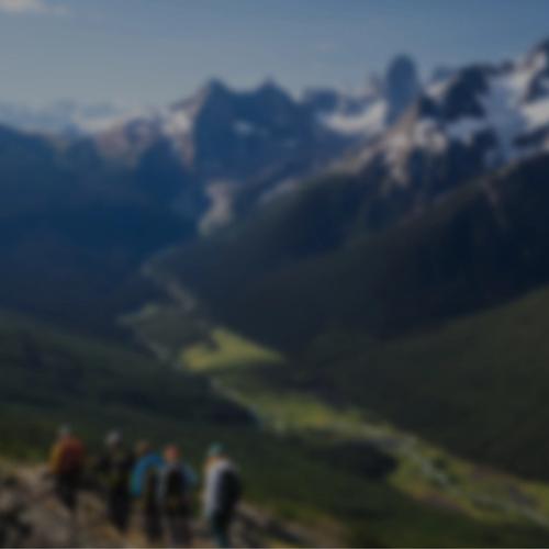 A group of people walking on a ridge with lush forest and a river below and mountains in the background