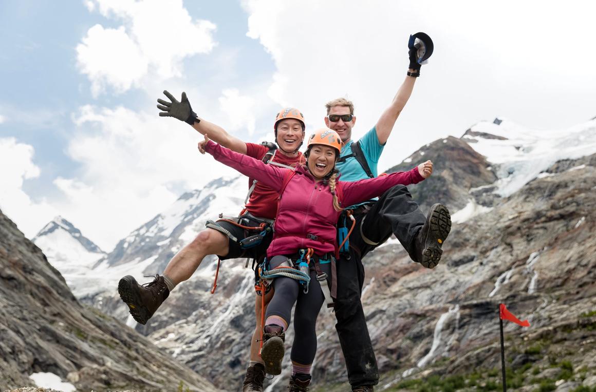 Looking up at 3 people with their arms up and mountains in the background