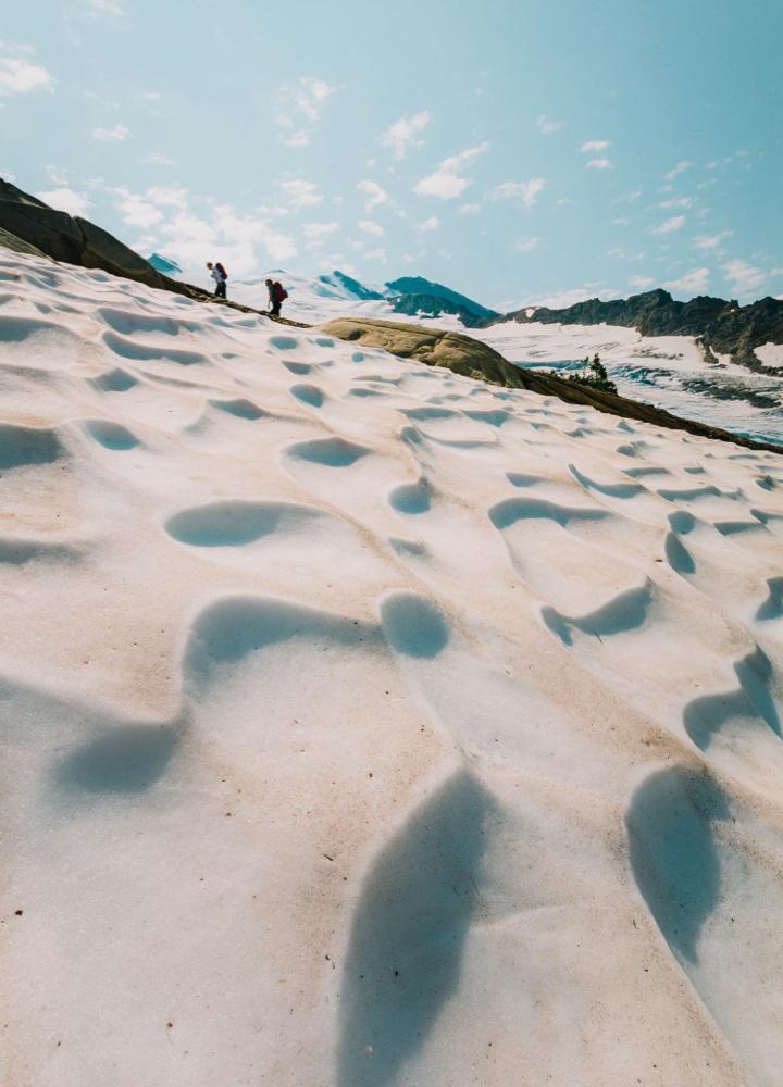 two people hiking in the distance with a wavy rock formation in the foreground