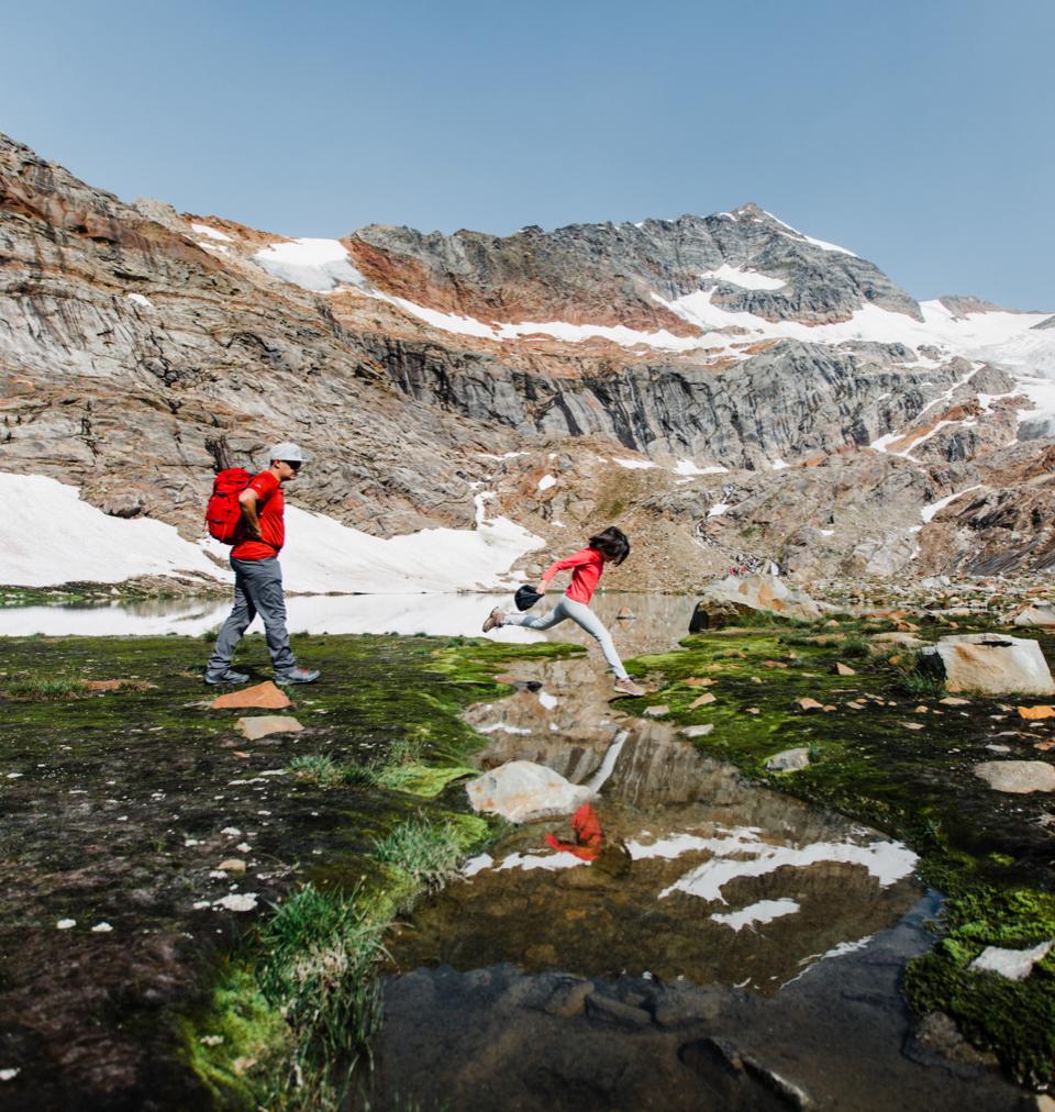 a child jumping across a stream with an adult following