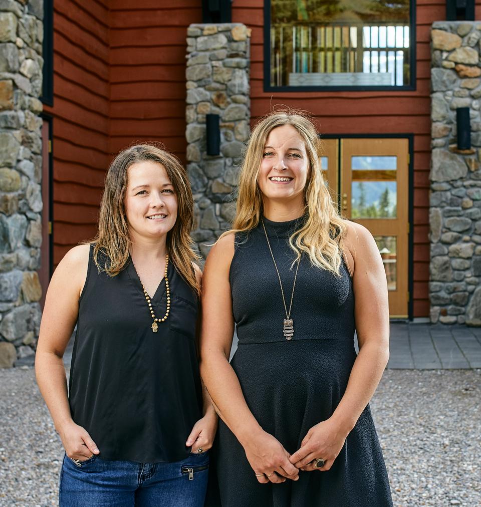 two women in black tops smiling in front of a lodge