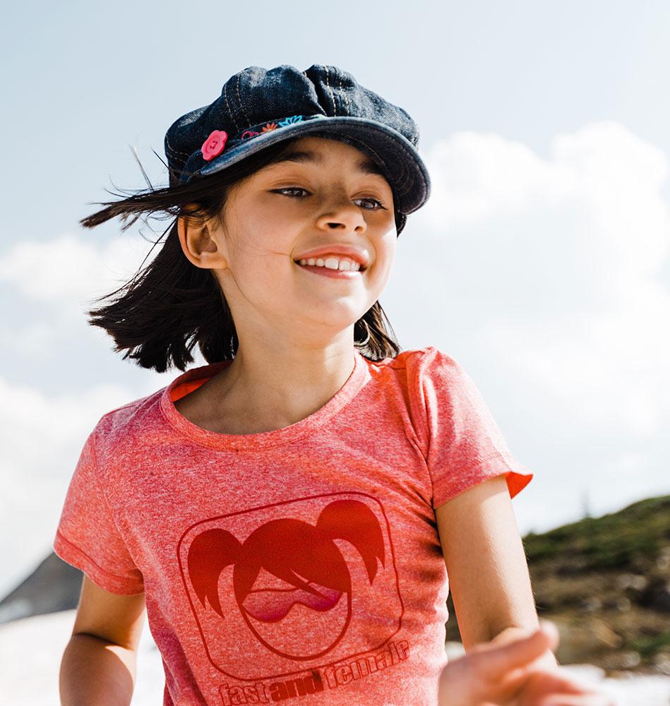 Smiling young girl wearing a denim cap and red shirt playing outdoors on a sunny day with blue sky in the background