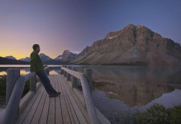 Person leaning on a dock looking out at a mountain in the evening