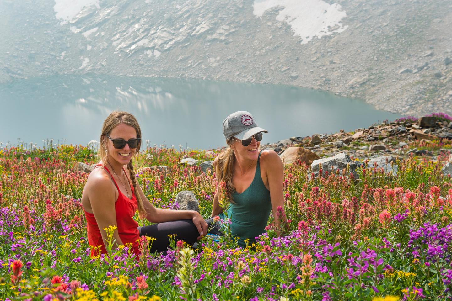 Two women sitting in a field of wild flowers with a lake in the background