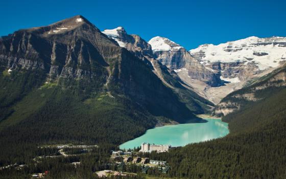 Arial shot of Lake Louise, huge mountains with lake below, and hotel at the base of the lake