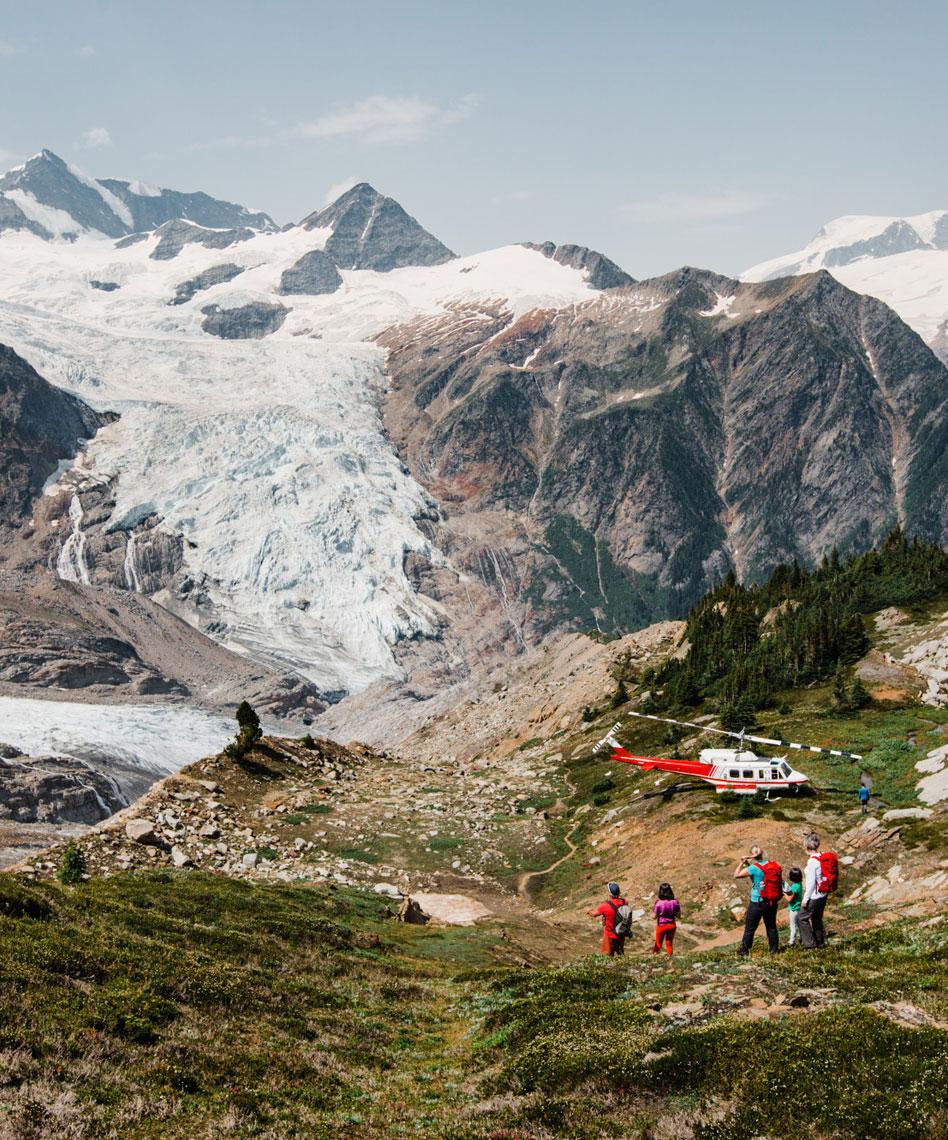 A group of people walking towards a helicopter with a glacier in the background