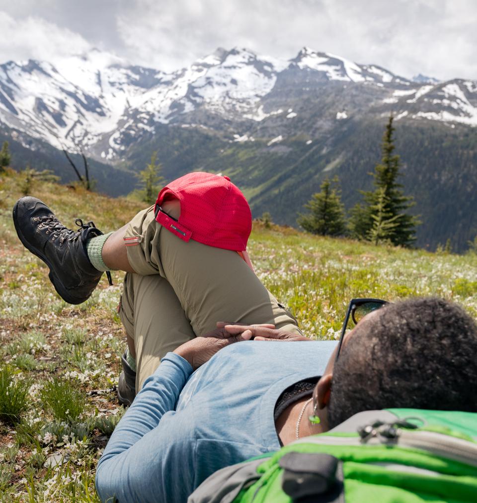A person laying down on their backpack with one leg over the other and a red cap on their knee