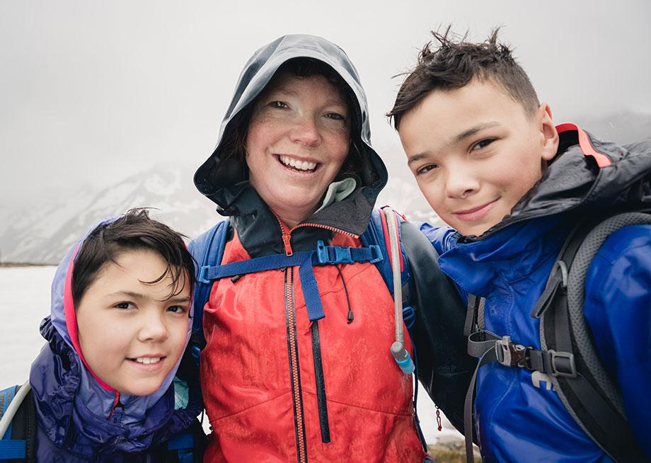 A woman smiling with her arms around two kids