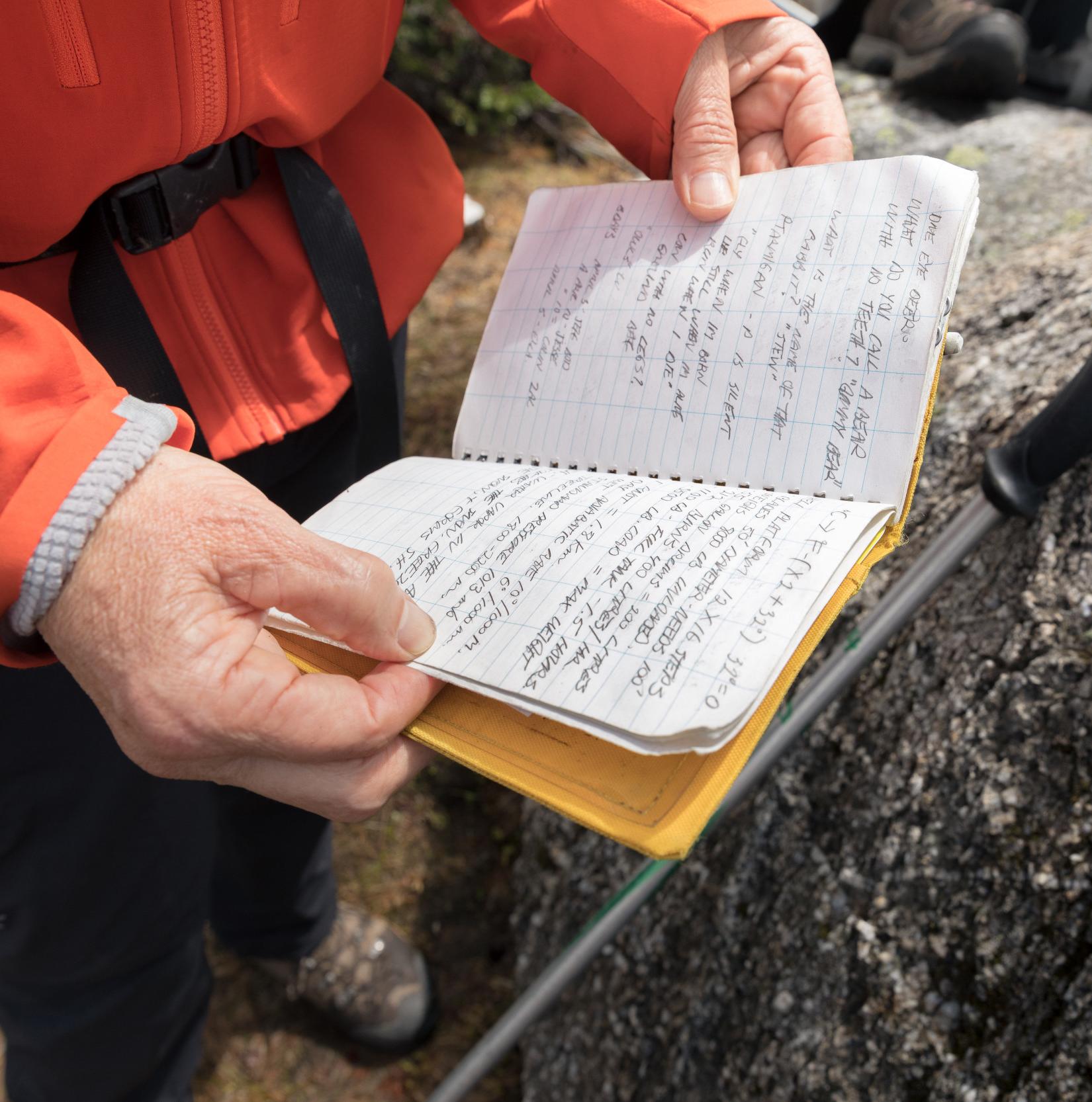 close up of a field notebook held by a person in an orange jacket against some rocks