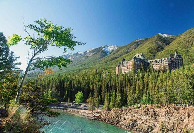 Image of a river in the foreground and the Banff spring hotel in the background surrounded by trees in front of mountains