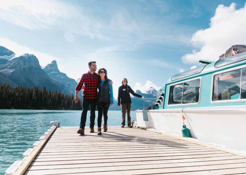 a couple with their arms around each other on a dock beside a water taxi with mountains in the background