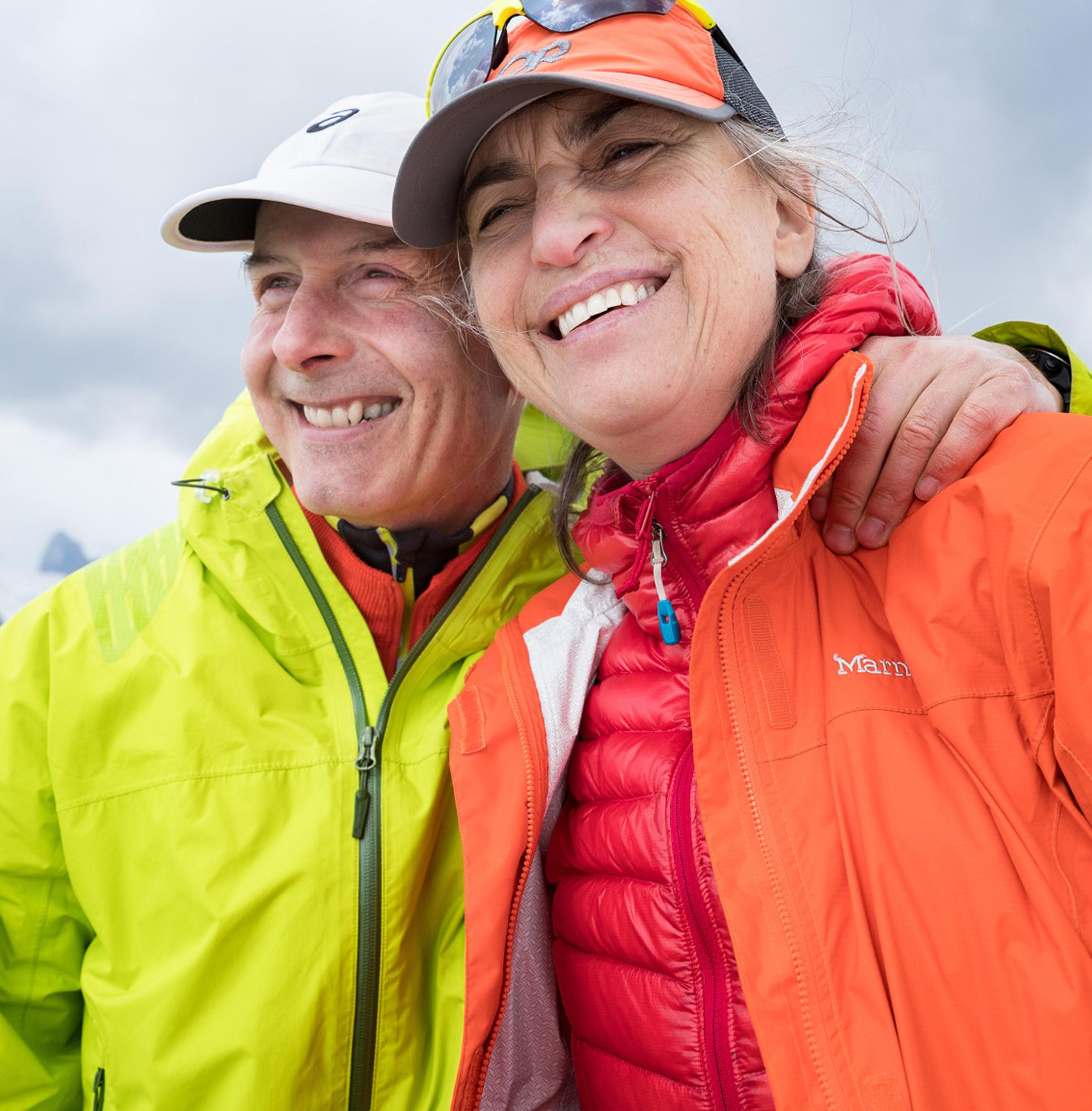 two friends smile with their arms around each other at a lookout at the end of a hike