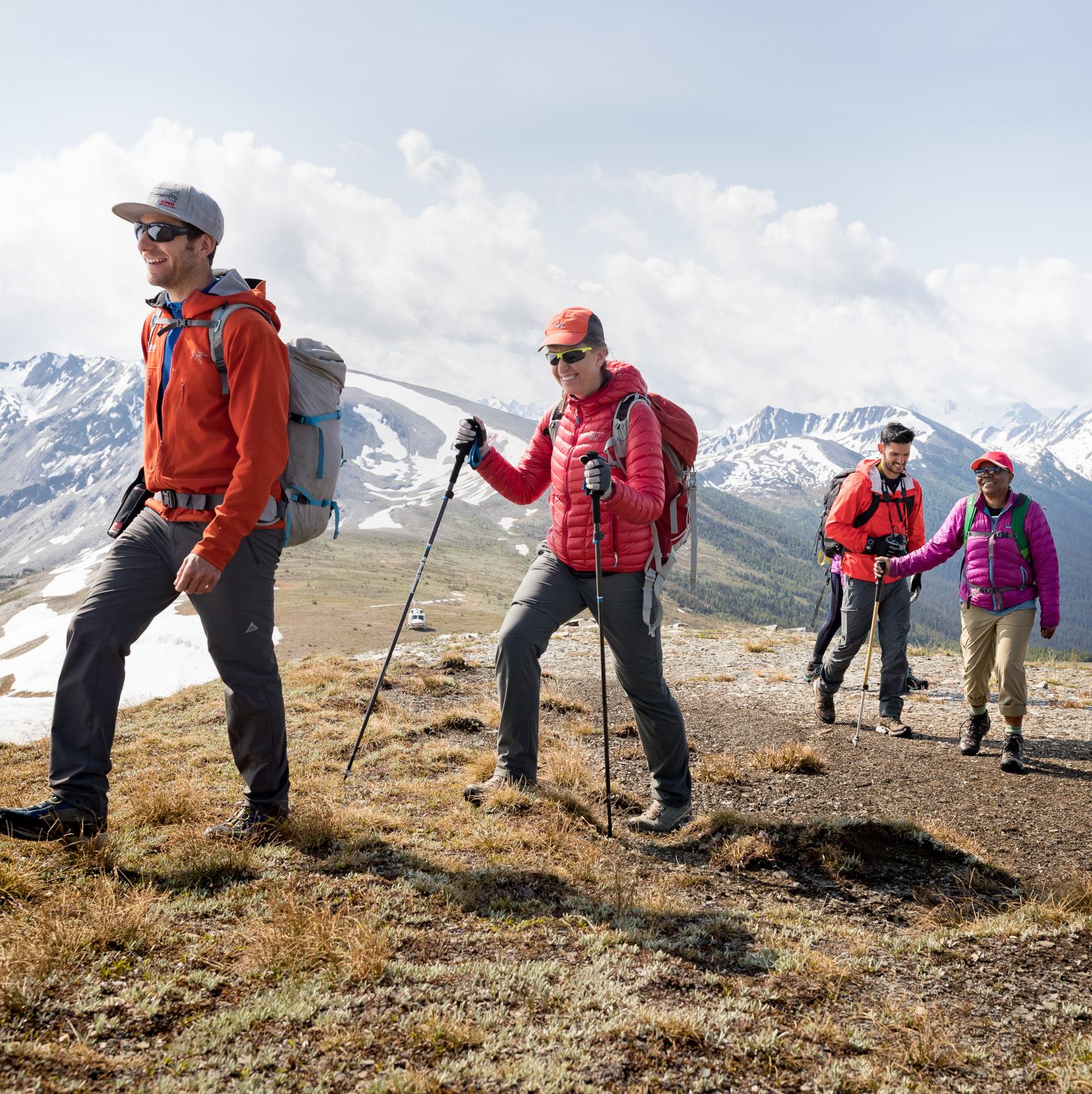 Four people walking in a row on a hill with mountains in the background