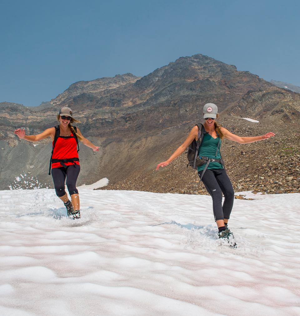 two women sliding in snow with a mountain in the background