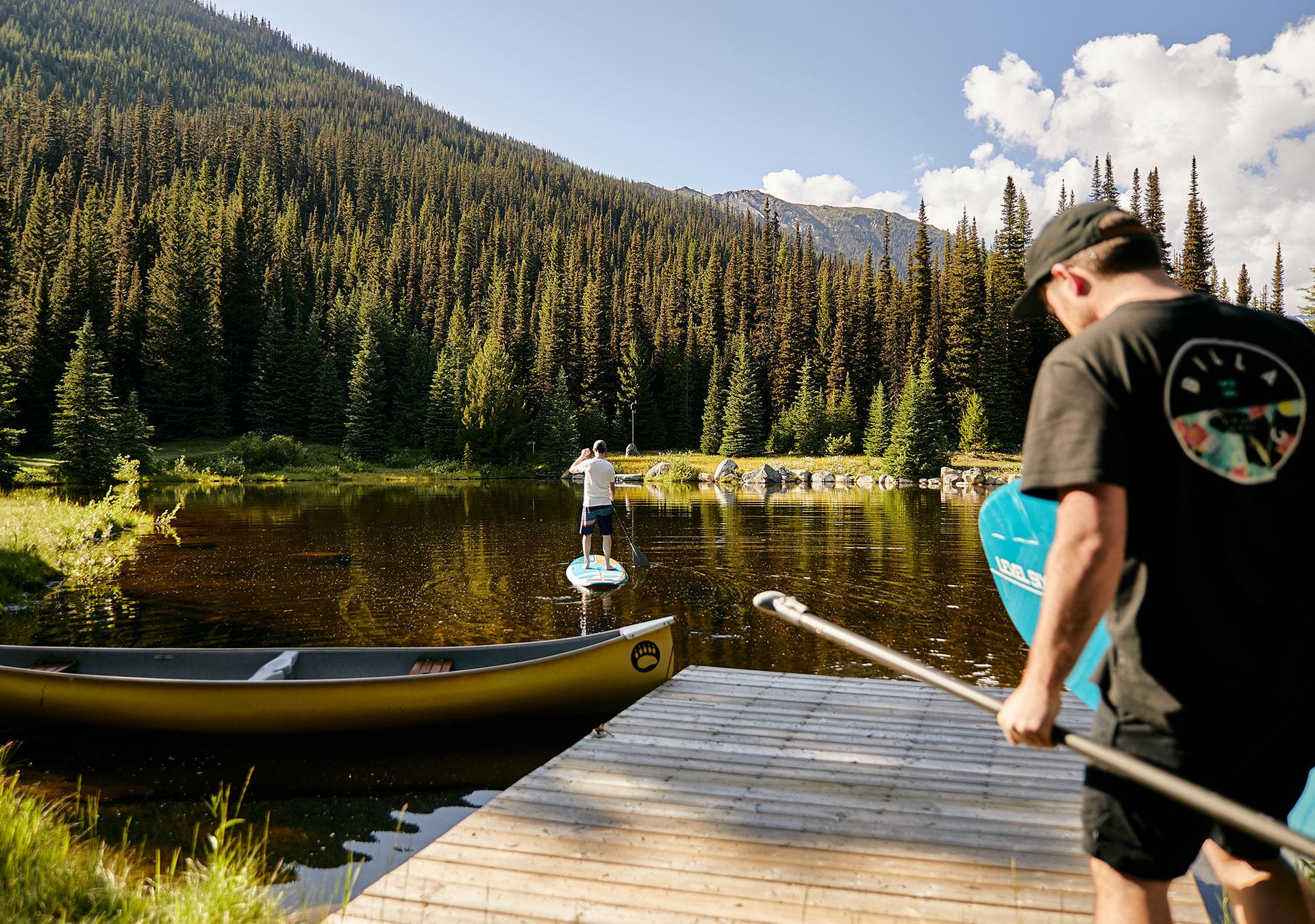 two friends enjoying a summer day on the lake. One is on the water on a standup paddle board while the other is on his way to join him.