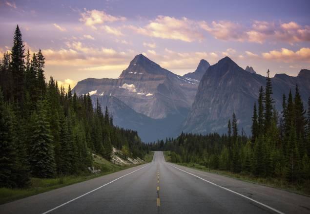 Looking down a highway at mountains at dusk with trees on either side