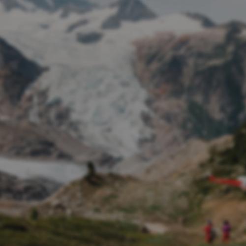 A group of people with a helicopter above and mountains in the background