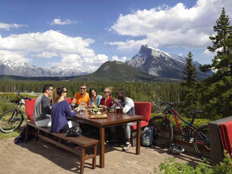 a group of people at a picnic table eating with trees and mountains in the background